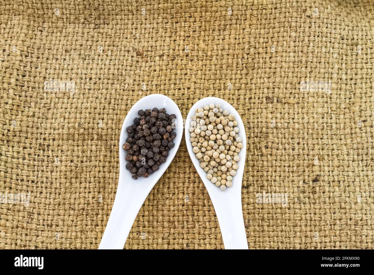 Close up black and white pepper in white ceramic spoon on fabric sack  background Stock Photo