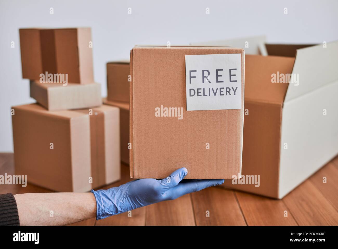 https://c8.alamy.com/comp/2FKMXRF/hand-in-glove-holding-a-cardboard-box-with-free-delivery-label-2FKMXRF.jpg