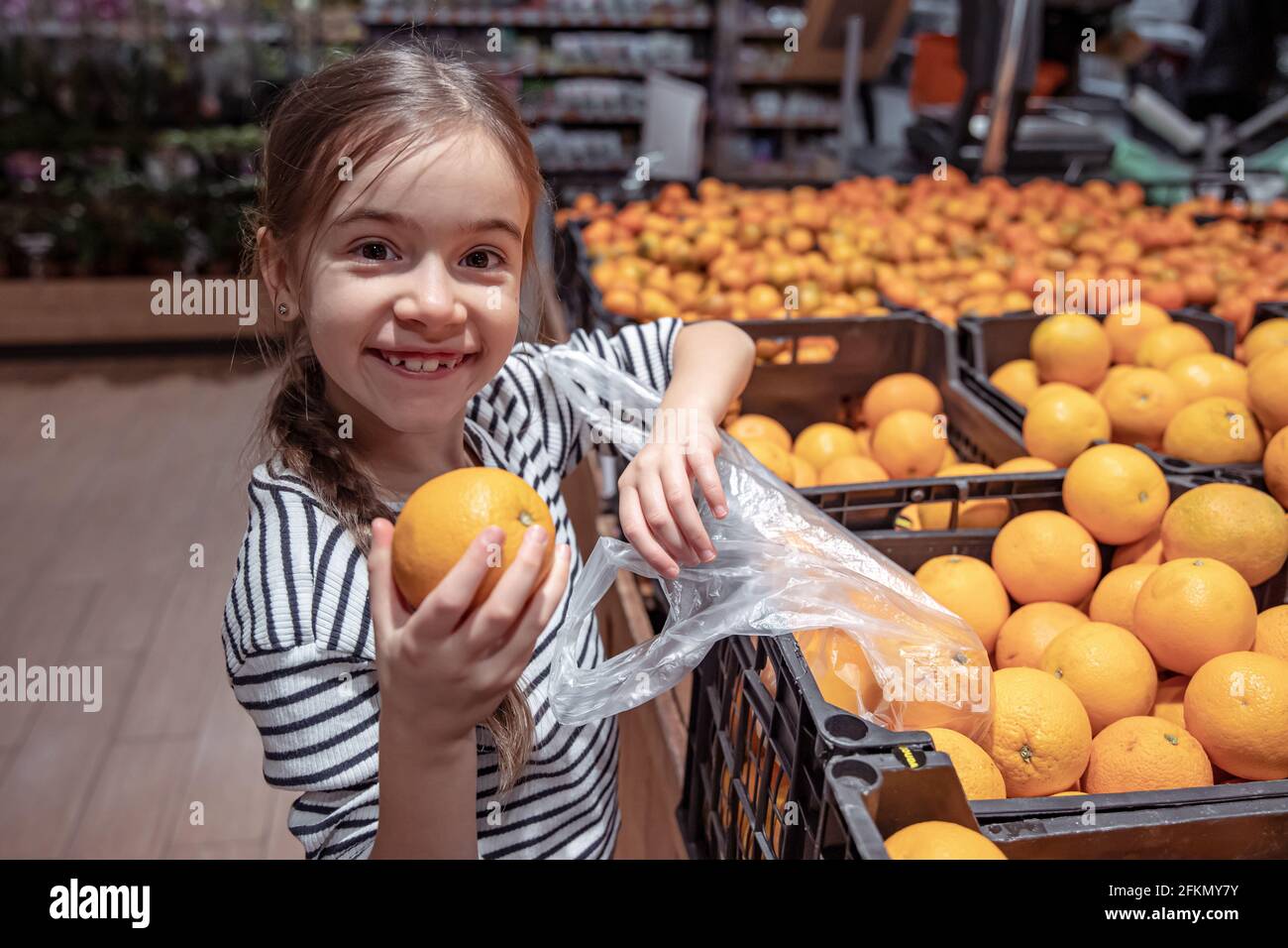 A funny little girl in a grocery store chooses oranges to buy Stock