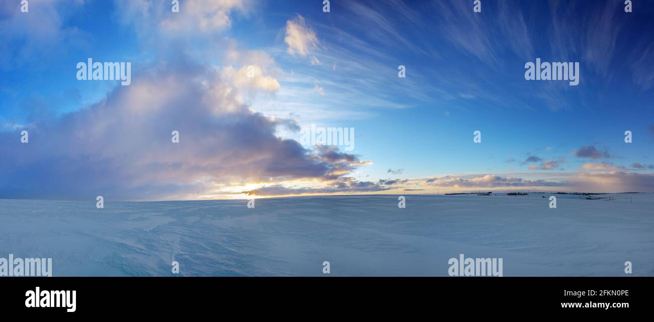 Beautiful panoramic landscape with dramatic clouds in blue sky over the snow covered field.Sunrise scenery. Stock Photo