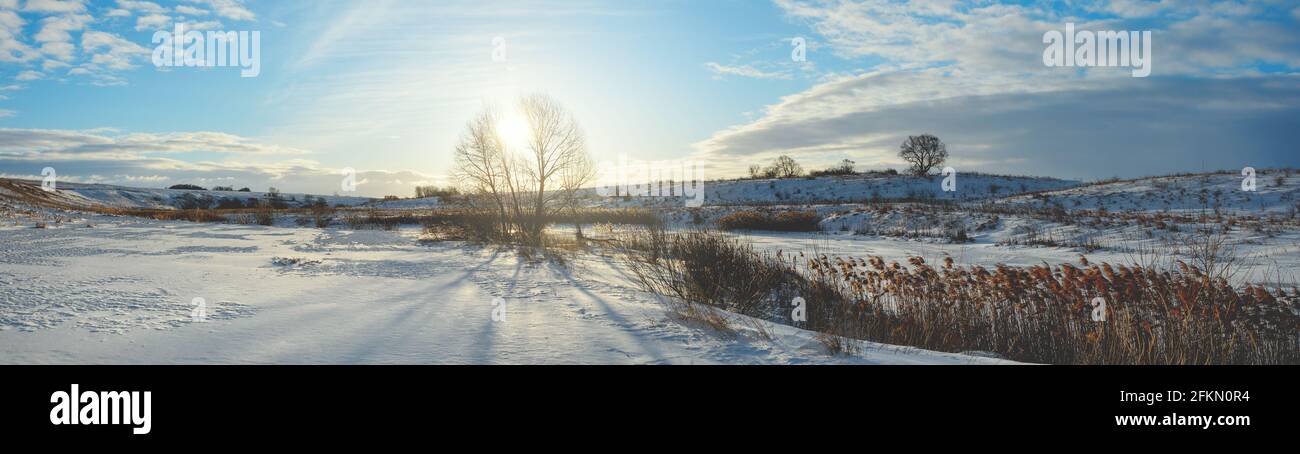 Sunny panoramic early springtime landscape.Beautiful view of frozen river and snow covered fields during sunny march morning. Stock Photo