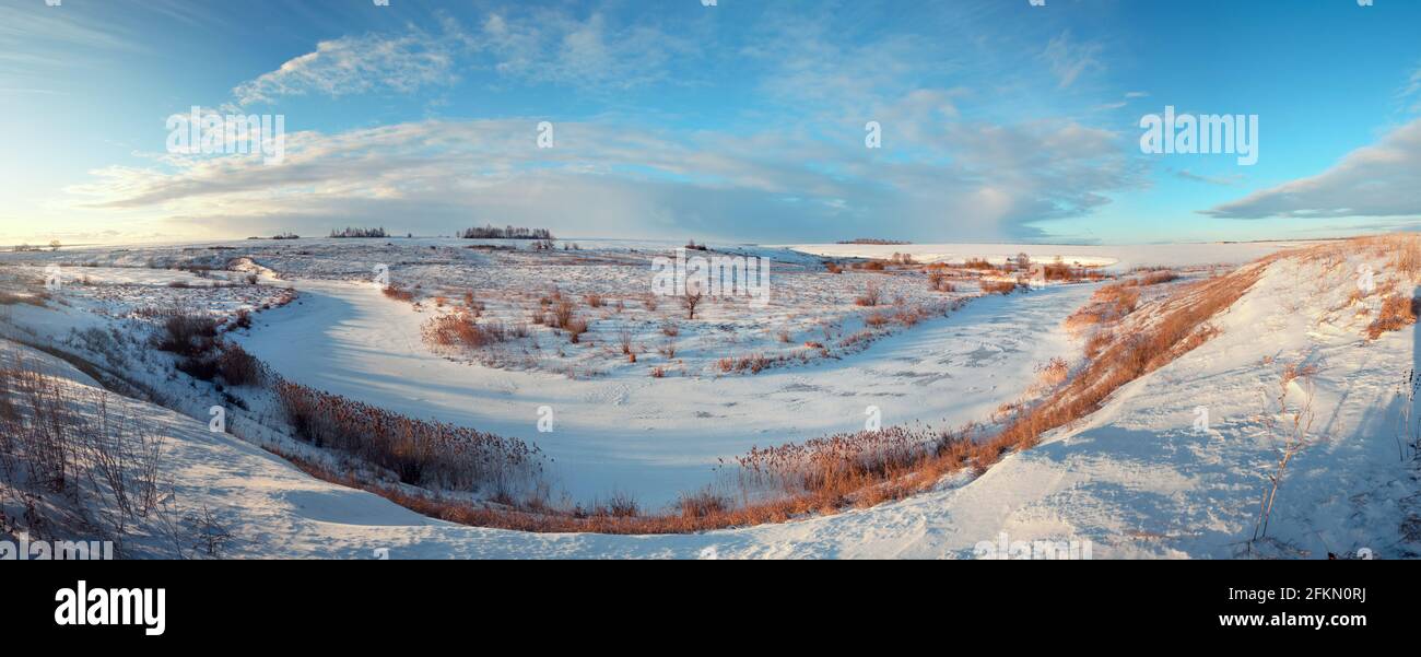 Sunny panoramic early springtime landscape.Beautiful view of frozen river and snow covered fields during sunny march morning. Stock Photo