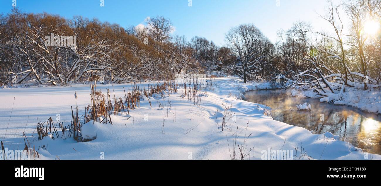Frosty winter panoramic landscape with snow coverd forest lawn and forest river during sunny january morning. Stock Photo