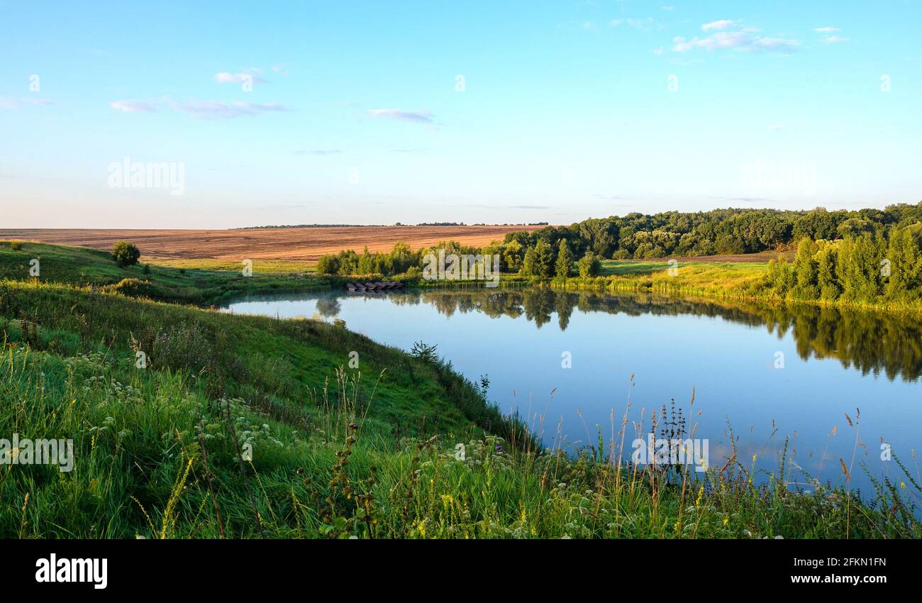Summer serene landscape with calm river and green hills at sunrise. Stock Photo