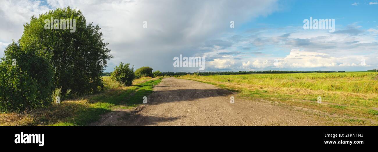 Sunny summer landscape with dirt rural road passing through the fields and meadows. Stock Photo