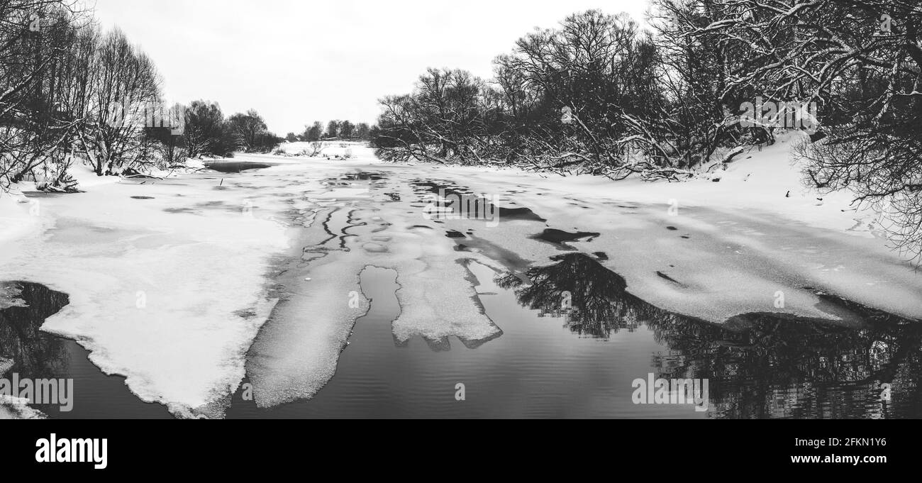 Black and white panoramic rural winter or springtime landscape with floating on water surface pieces of melting ice Stock Photo