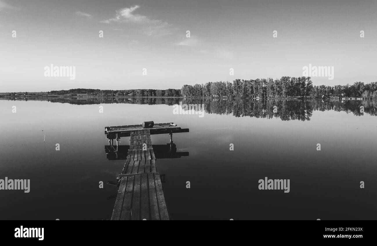 Black and white bright rural landscape with wooden jetty and calm lake during summer morning Stock Photo