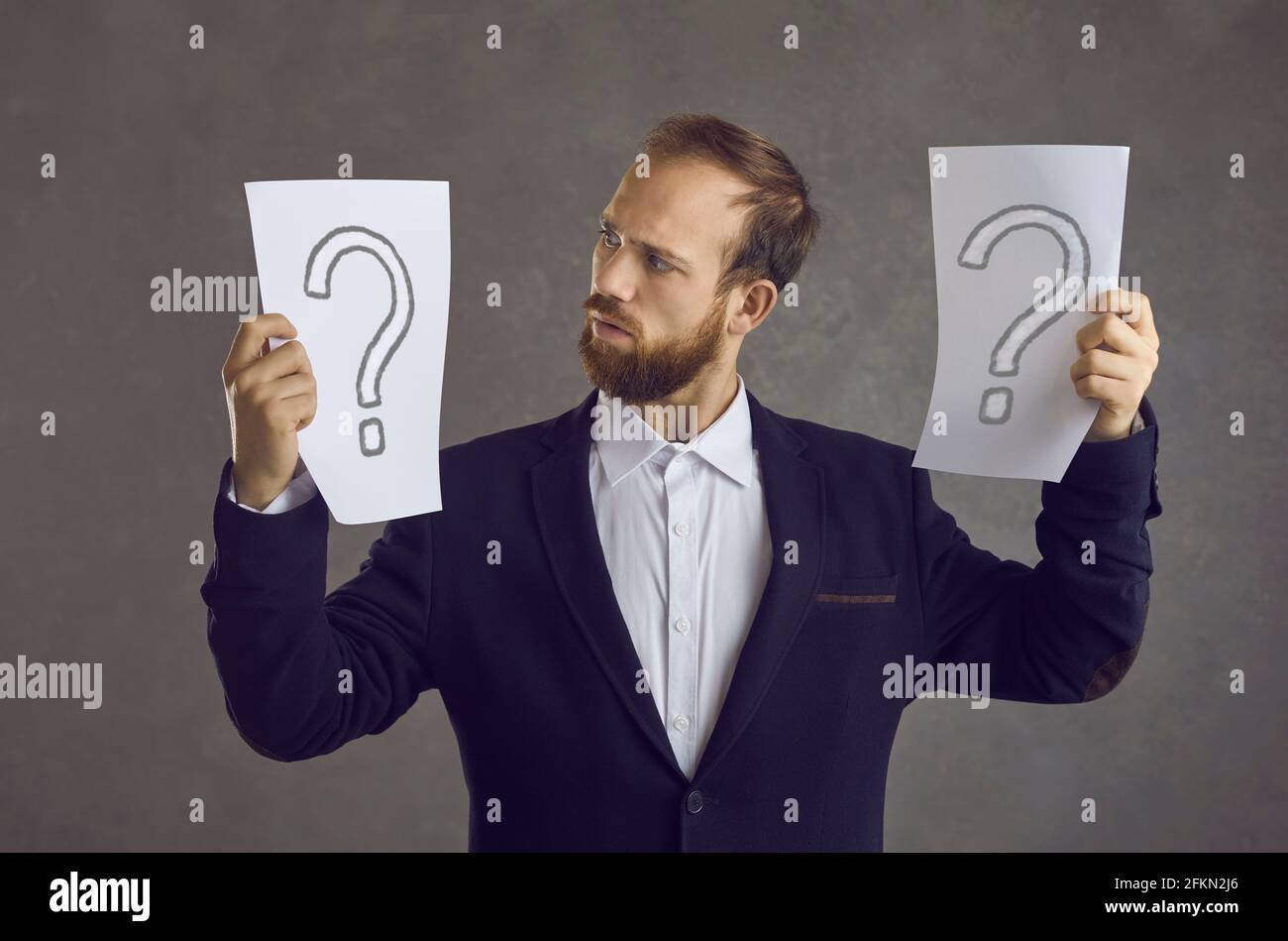 Puzzled businessman holding two question marks asking himself what decision to take Stock Photo