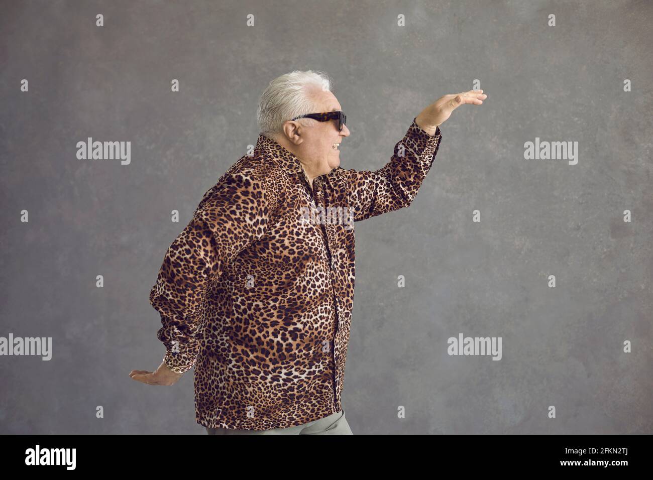 Side view of funny senior man in leopard shirt dancing in studio with gray background Stock Photo