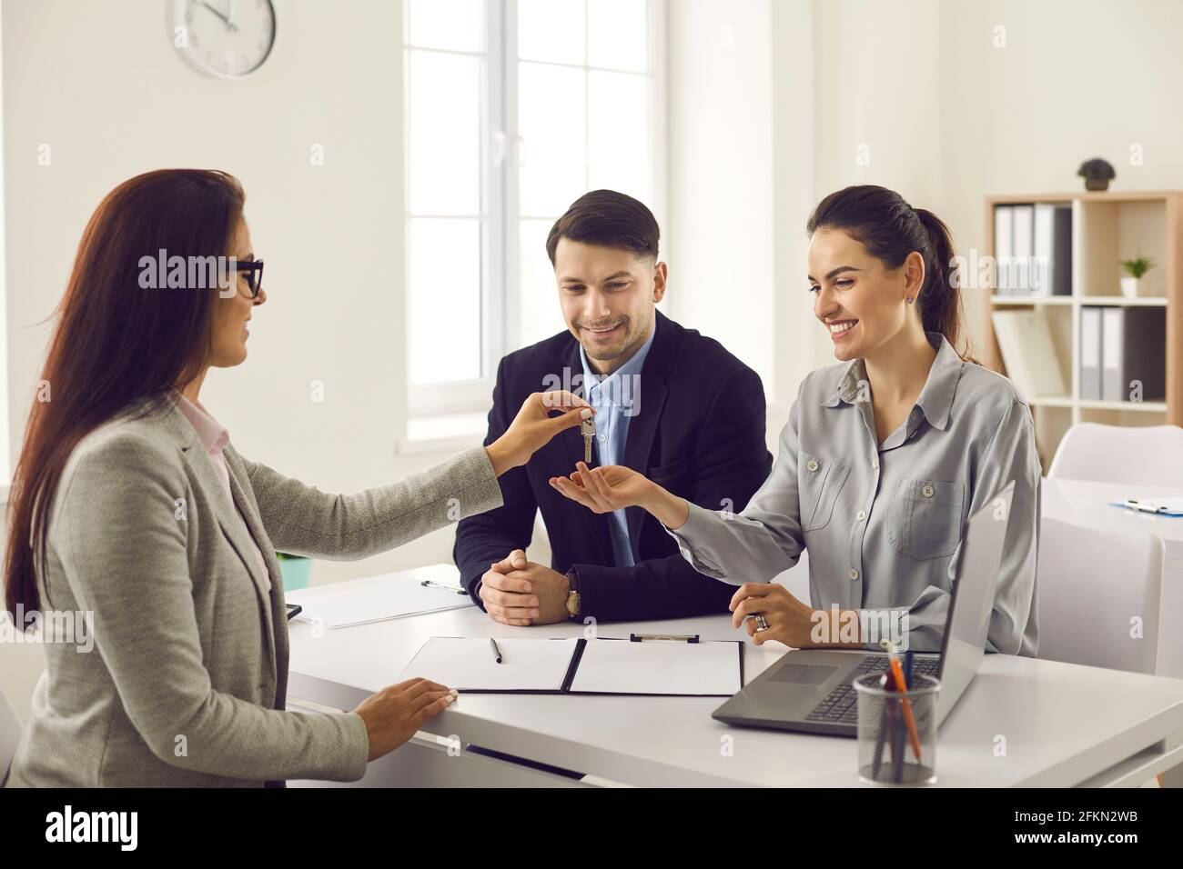 Real estate agent gives the keys to her new home to a married couple at a meeting in the office. Stock Photo