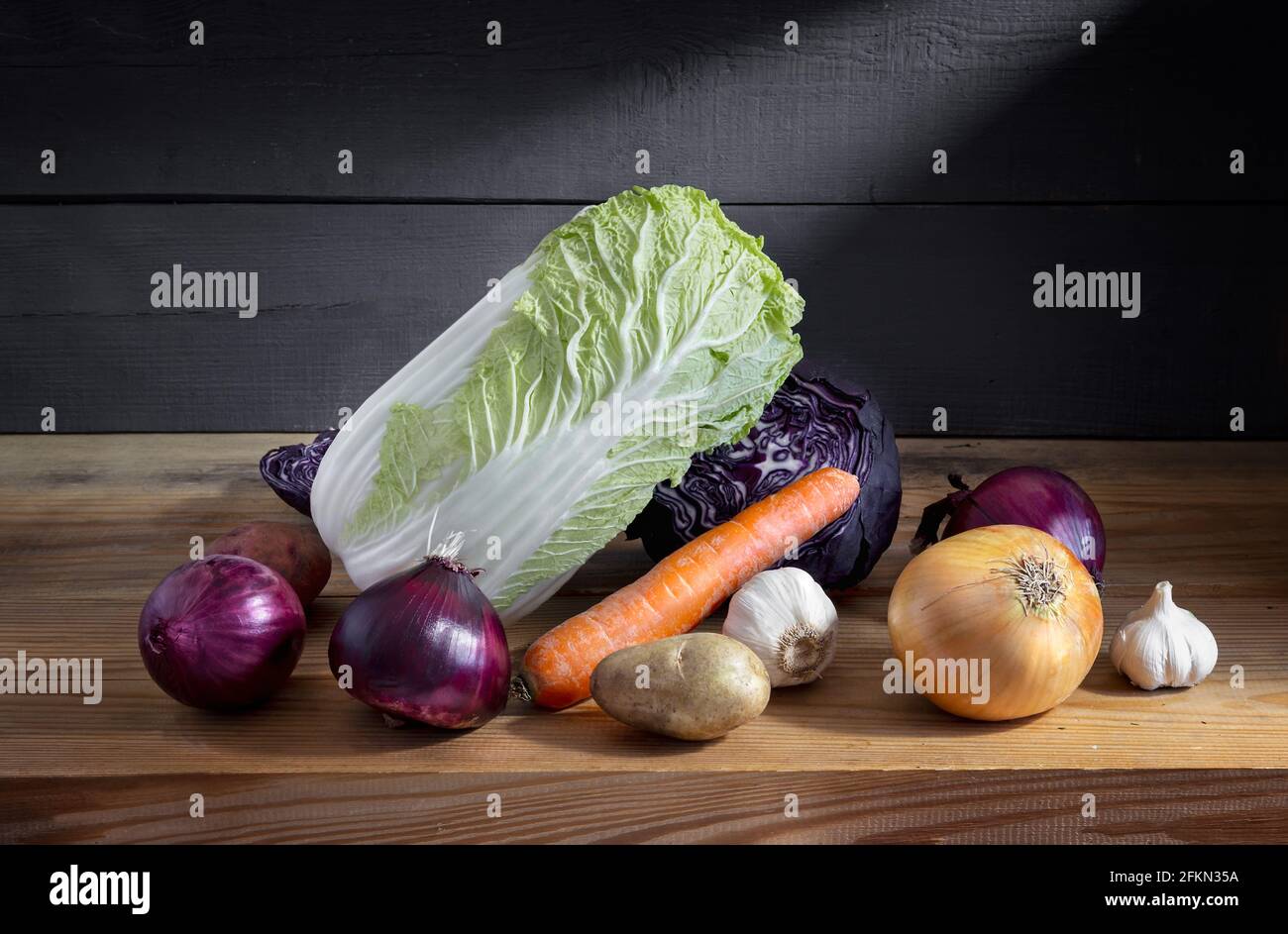 Still life: on a wooden shelf in the basement lies carrots, onions, red and white cabbage. Front view, copy space Stock Photo