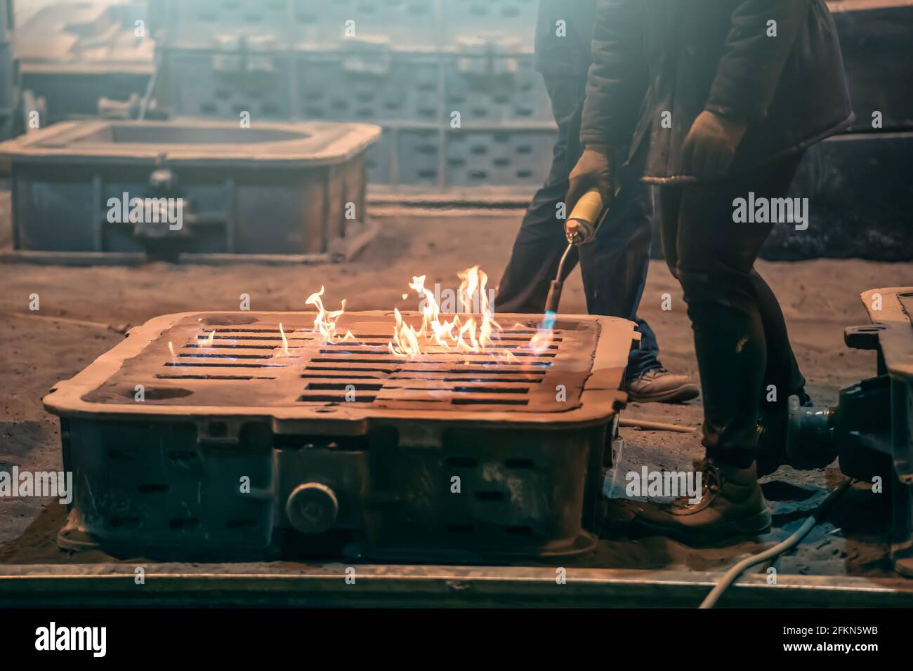 Worker burns mold container with fire after smelting metal close up. Stock Photo