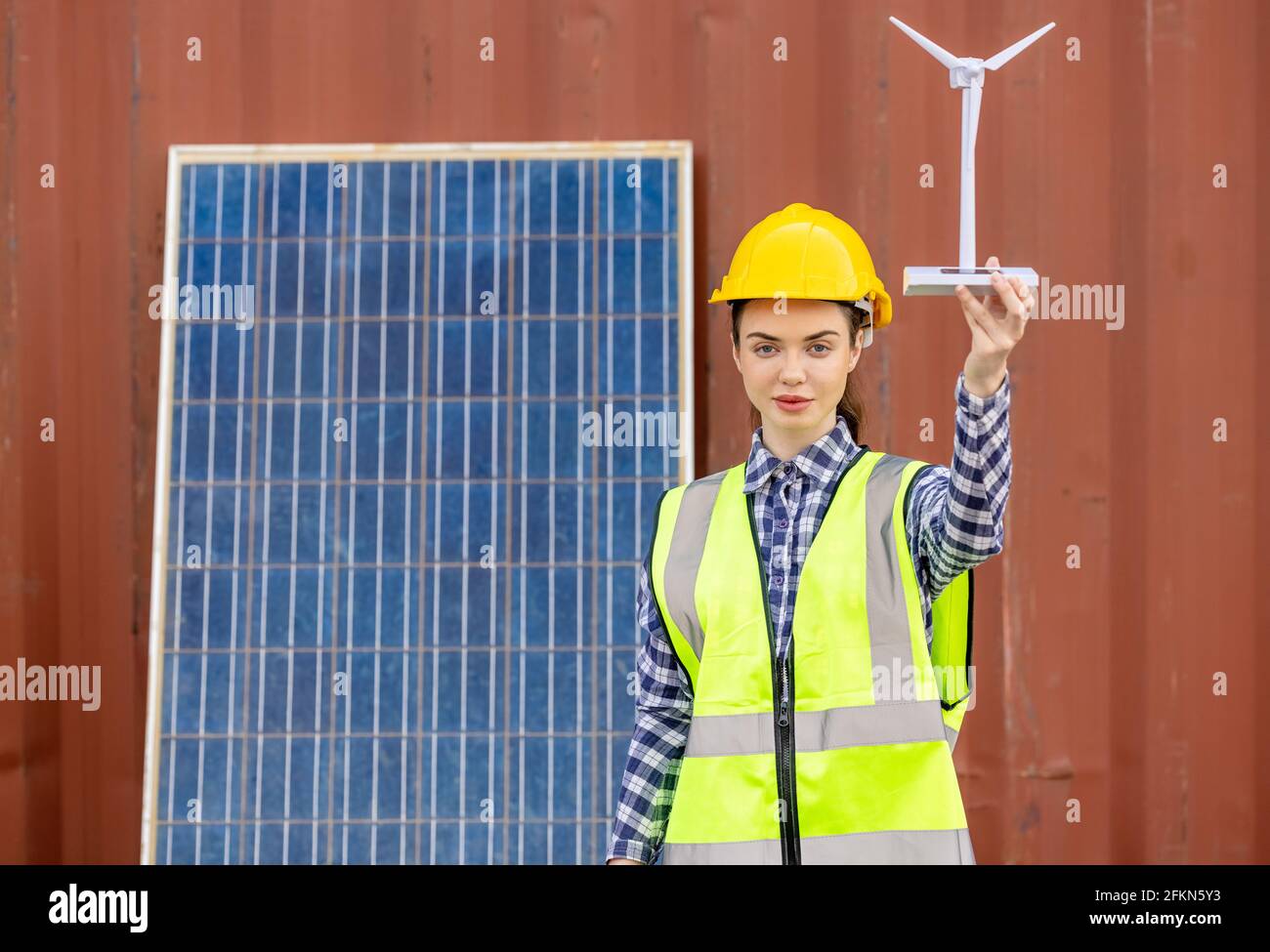 factory workers or engineers holding light bulb and using tablet computer with windmill model on solar panel,  work in containers warehouse storage Stock Photo