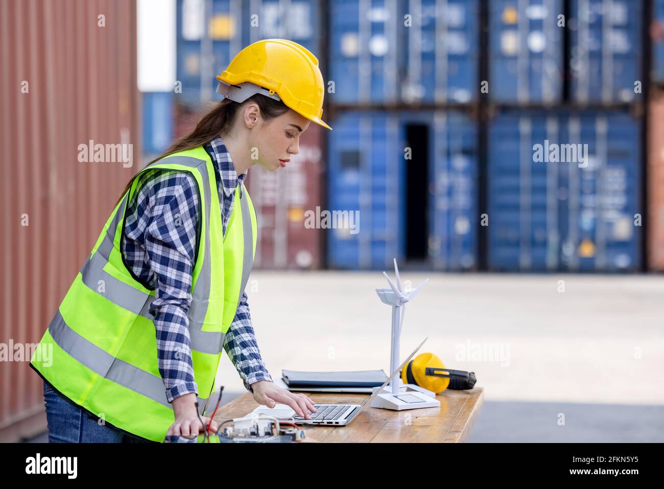 factory workers or engineers holding light bulb and using tablet computer with windmill model on solar panel,  work in containers warehouse storage Stock Photo