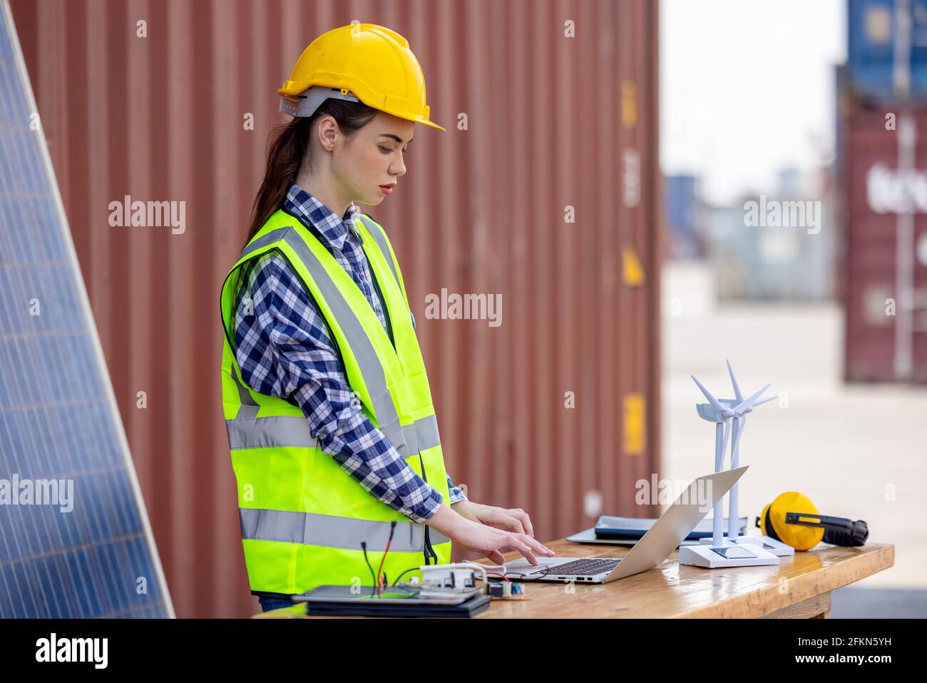 factory workers or engineers holding light bulb and using tablet computer with windmill model on solar panel,  work in containers warehouse storage Stock Photo