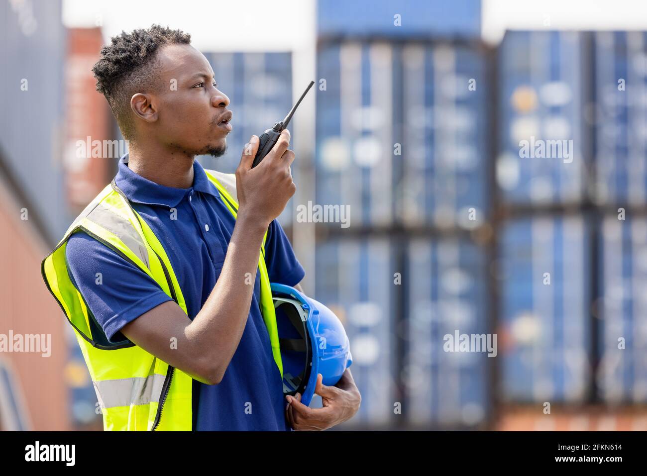 Man Using Walkie Talkie At Container Terminal, Industrial worker is controlling container loading Stock Photo
