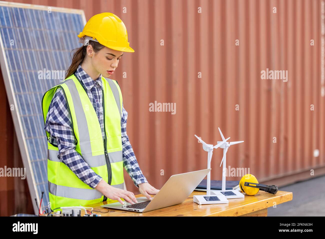 factory workers or engineers holding light bulb and using tablet computer with windmill model on solar panel,  work in containers warehouse storage Stock Photo