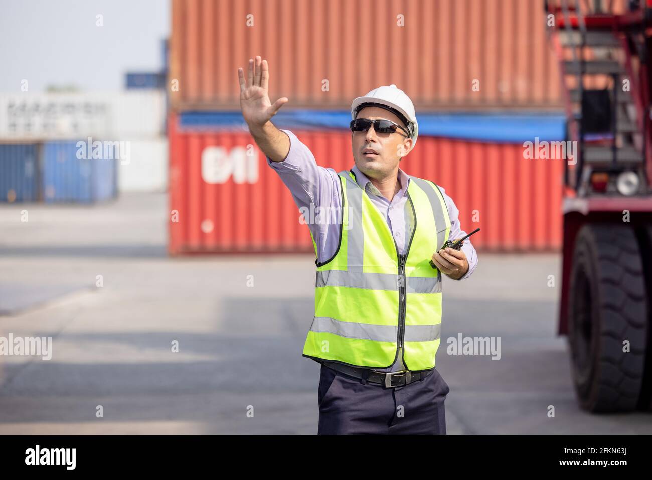 Man Using Walkie Talkie At Container Terminal, Industrial worker is controlling container loading Stock Photo