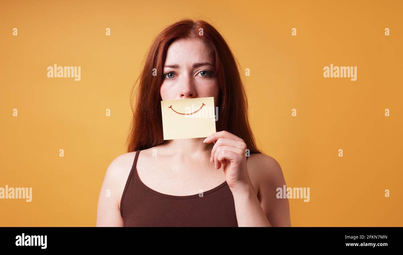 young woman hiding emotion with fake smile drawn on paper Stock Photo