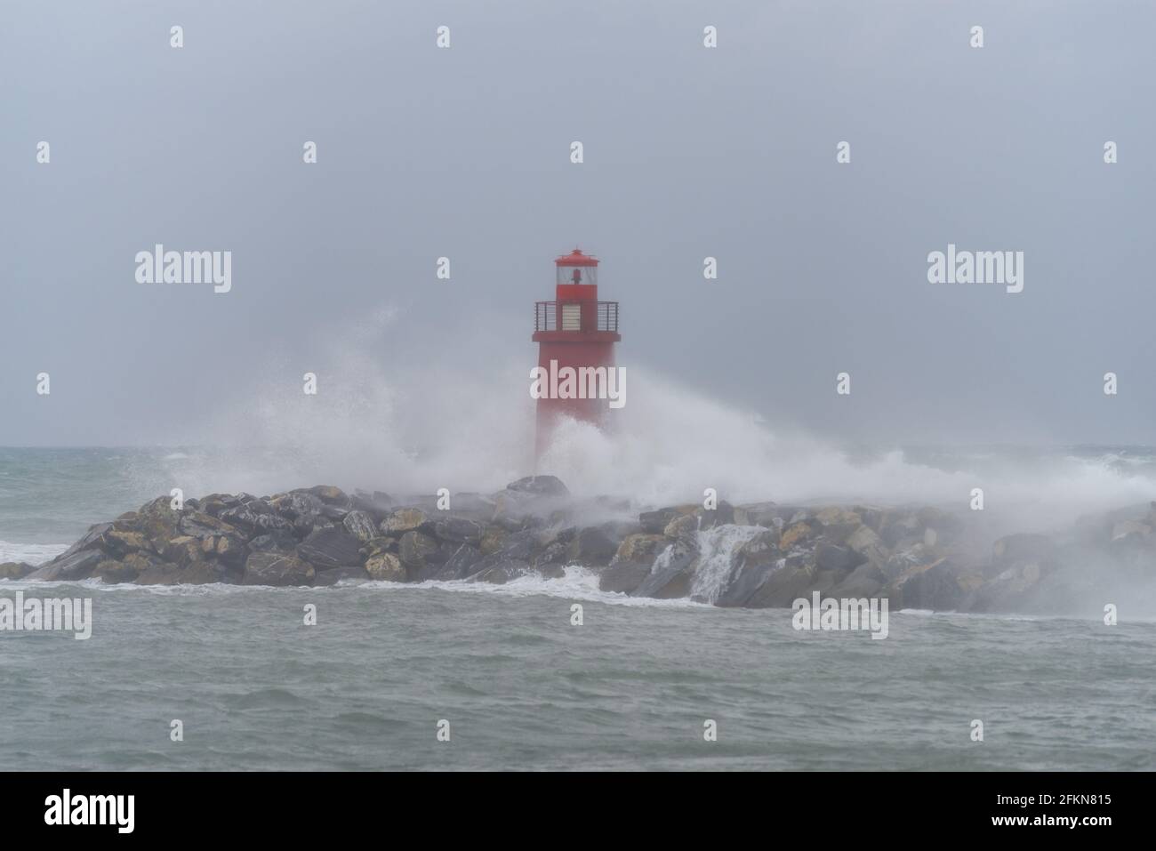 Waves crashing on breakwater with lighthouse in Imperia harbour, Italy Stock Photo