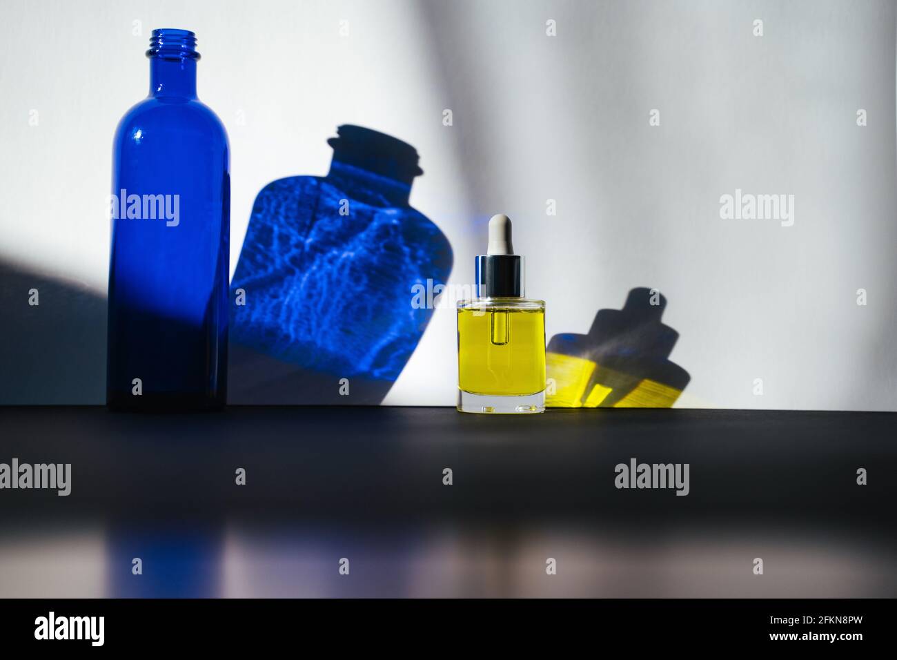 Dark blue glass bottle and face oil in front of white background. Shadows in direct sunlight. Side view Stock Photo
