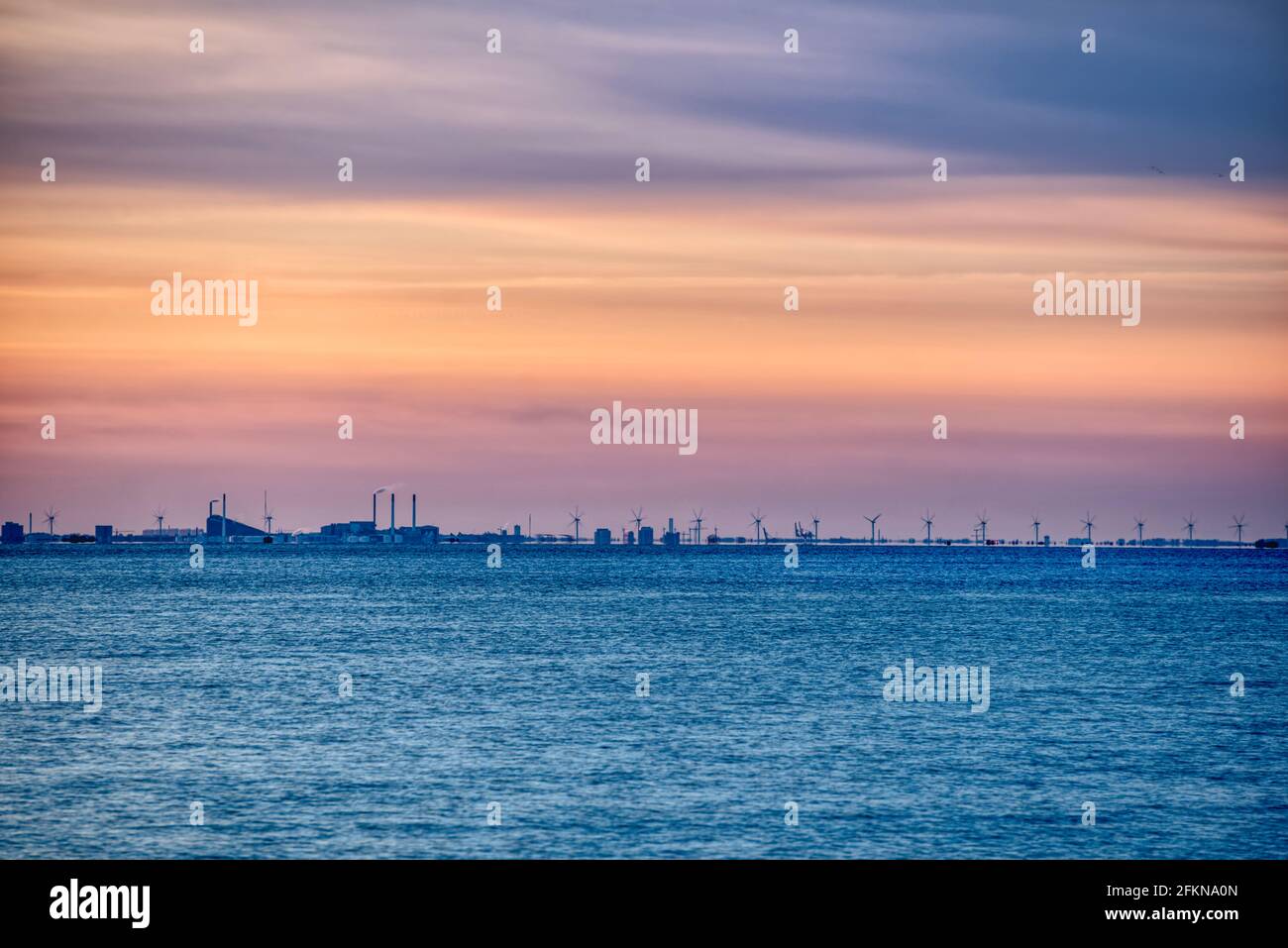 Copenhagen skyline at sunset with turbines rotating away in the Danish wind farm. Baltic Sea wind power plant with the city 's industrial skyline Stock Photo