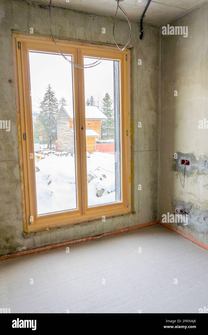Interior of a new apartment with windows under construction without finishing in dark tones with electrical holes and wiring for ceiling spotlight. Hi Stock Photo