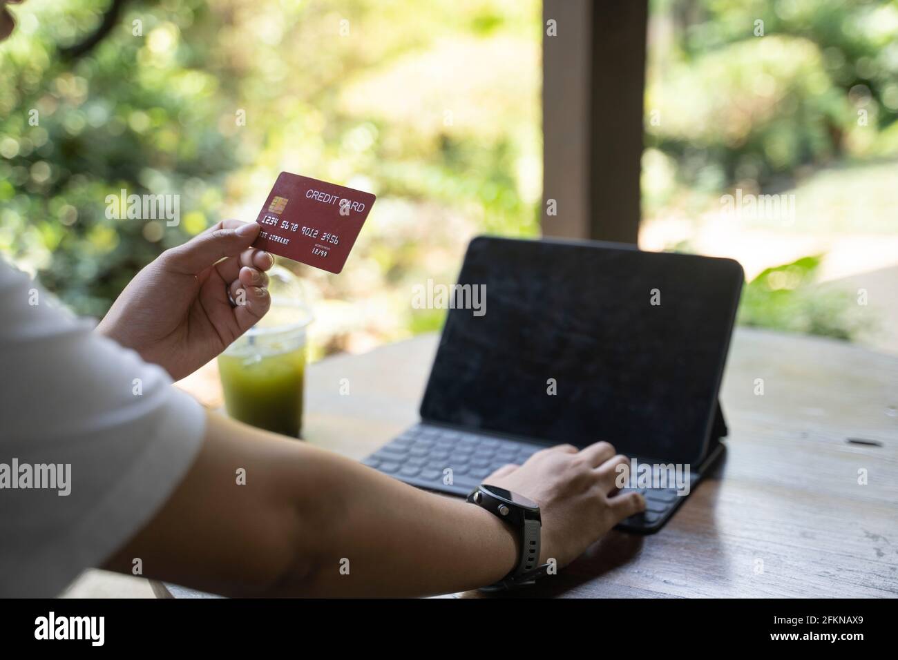 Asian woman sitting on the floor by the sofa, shopping online with laptop and entering credit card details for payment at home. Stock Photo