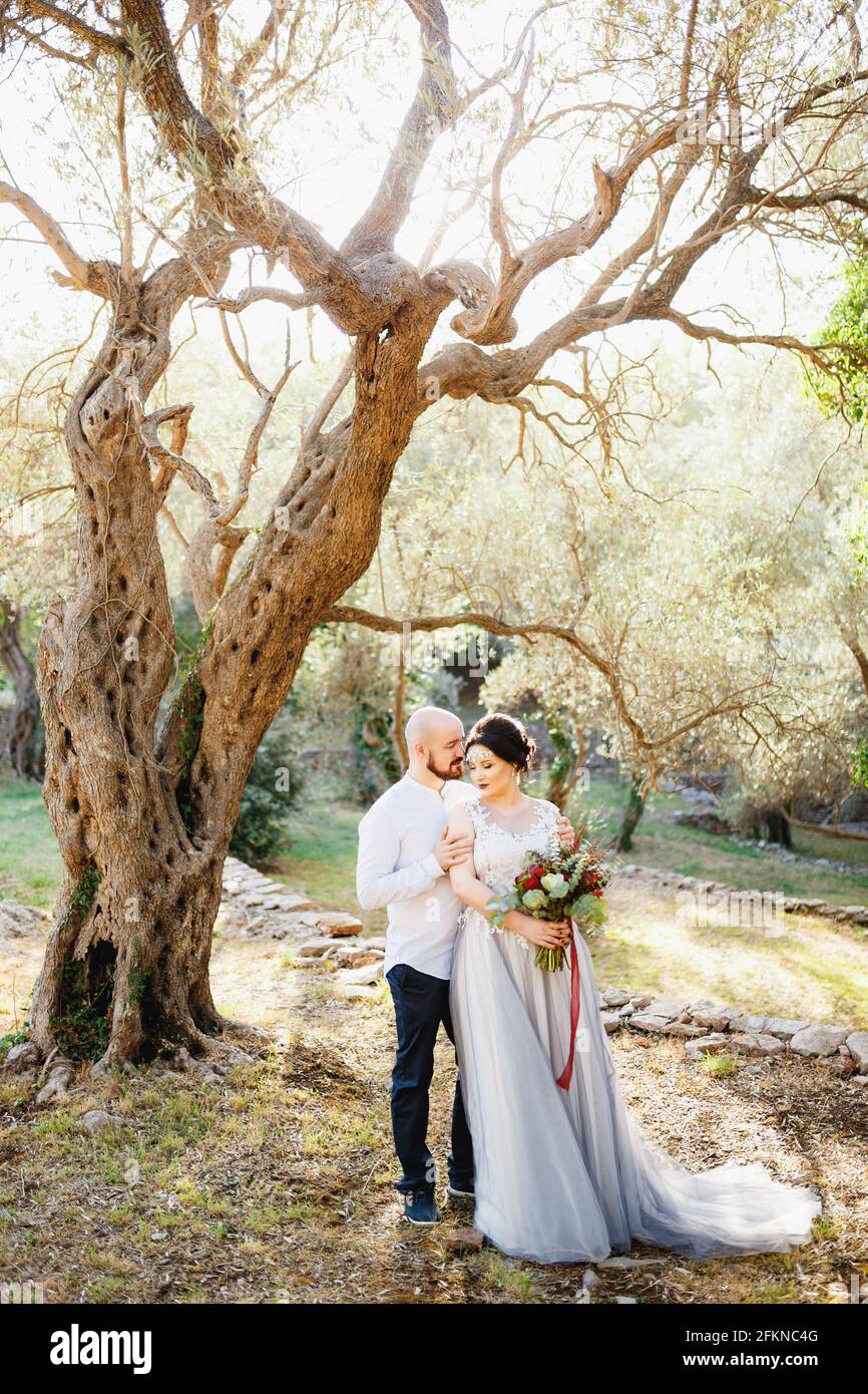 The bride and groom with a bouquet stand hugging among the trees in an ...