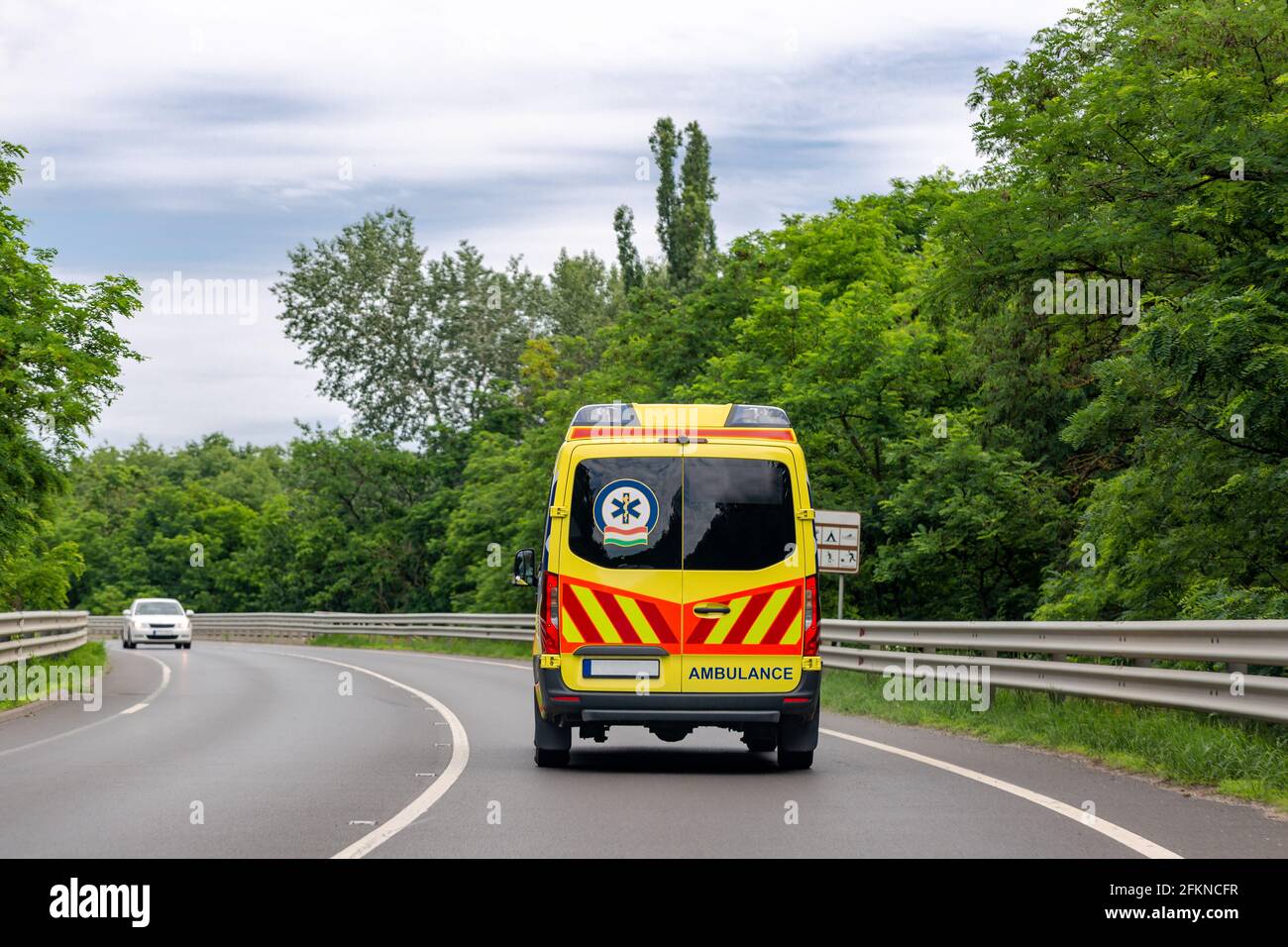 Ambulance van on the road. Bright green trees along road Stock Photo