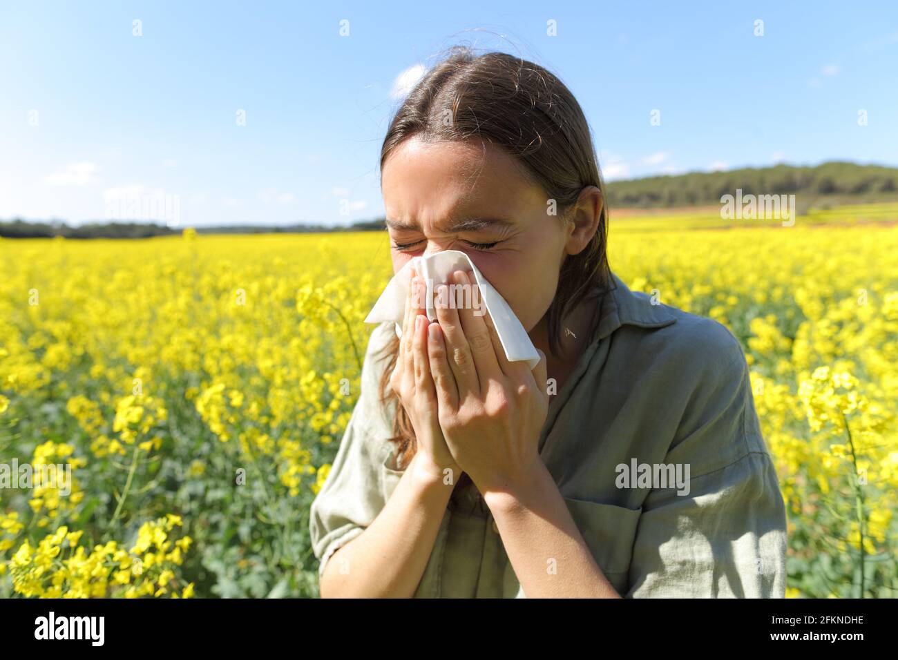 Woman suffering allergy coughing in a yellow flowered field in spring season Stock Photo