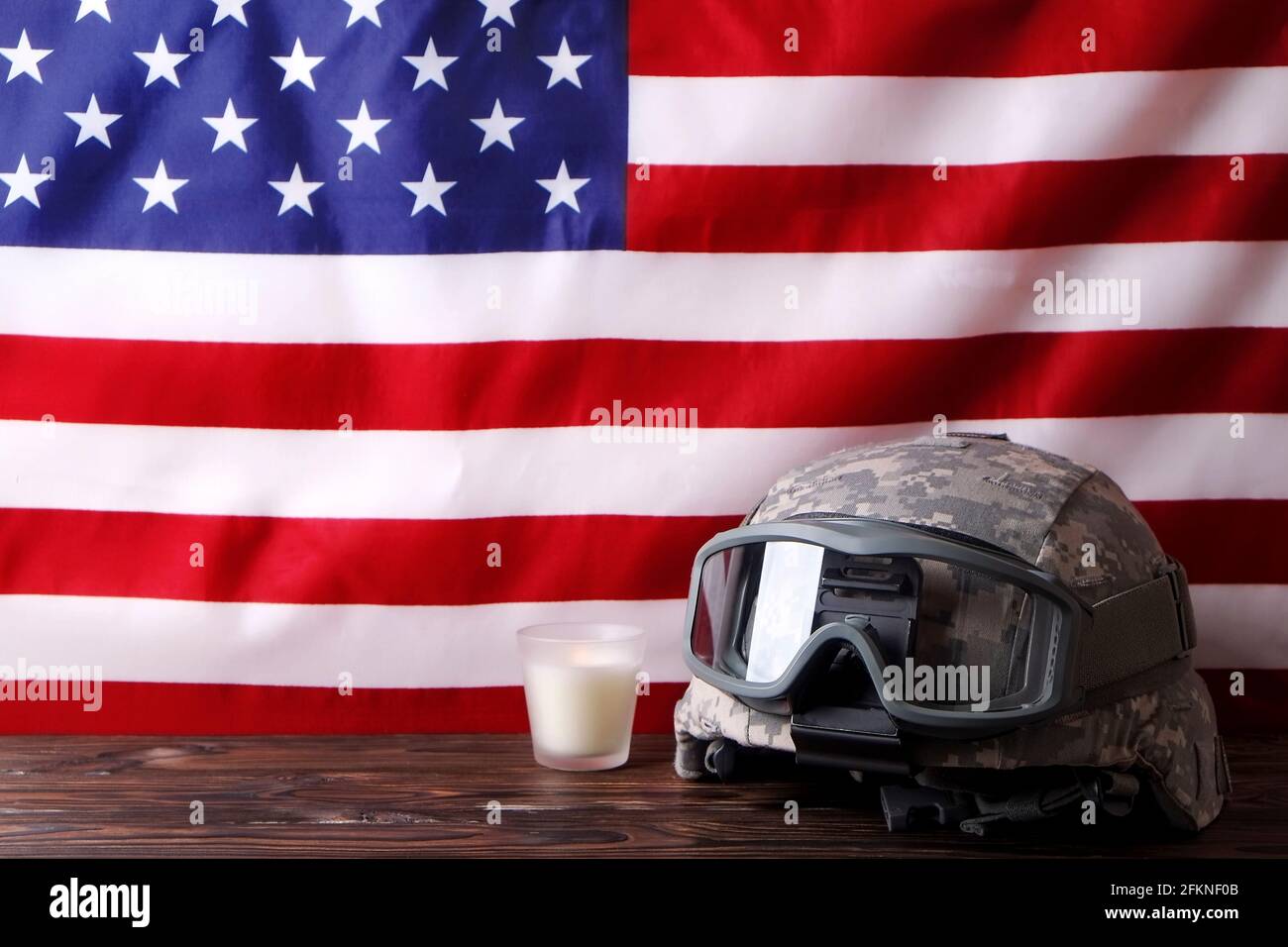 US Army kevlar combat helmet, camo cover, tactical goggles, candle USA flag background. Memorial weekend, veterans day, United States of America armed Stock Photo