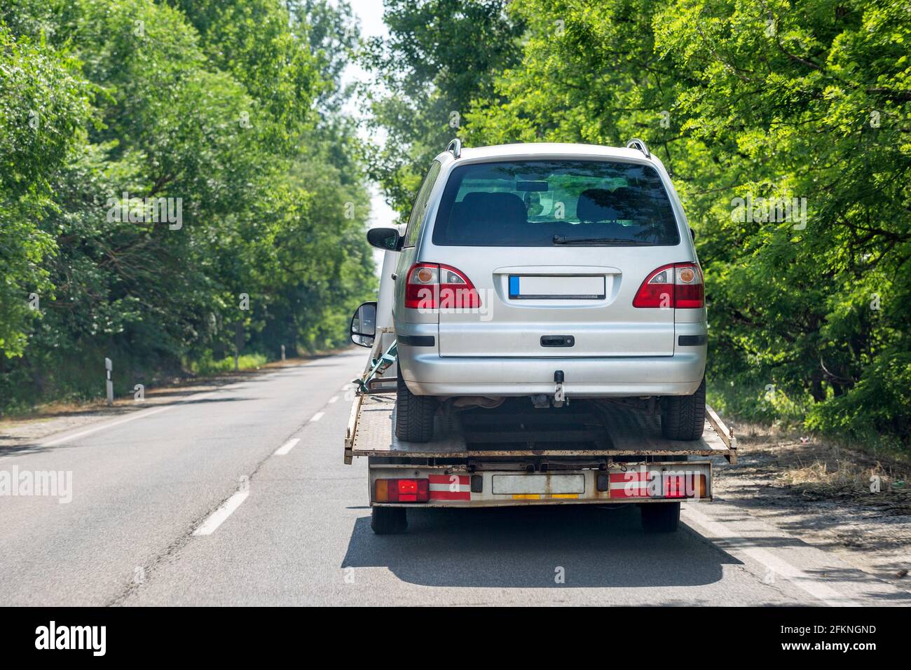 Truck transporter carrying car on the road. Back view. Bright green trees along road Stock Photo