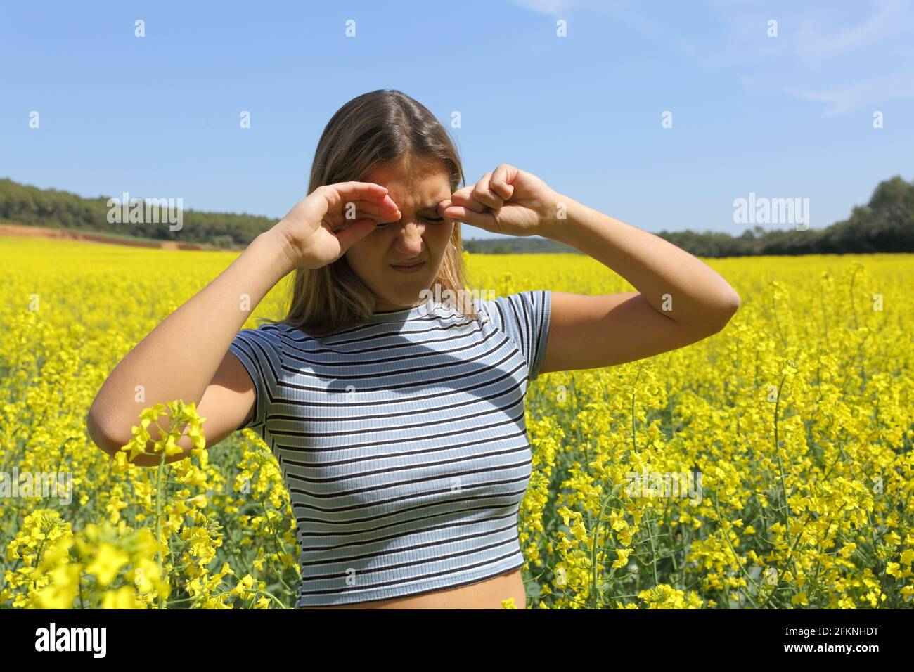 Stressed woman scratching itchy eyes in a crop field in spring season Stock Photo