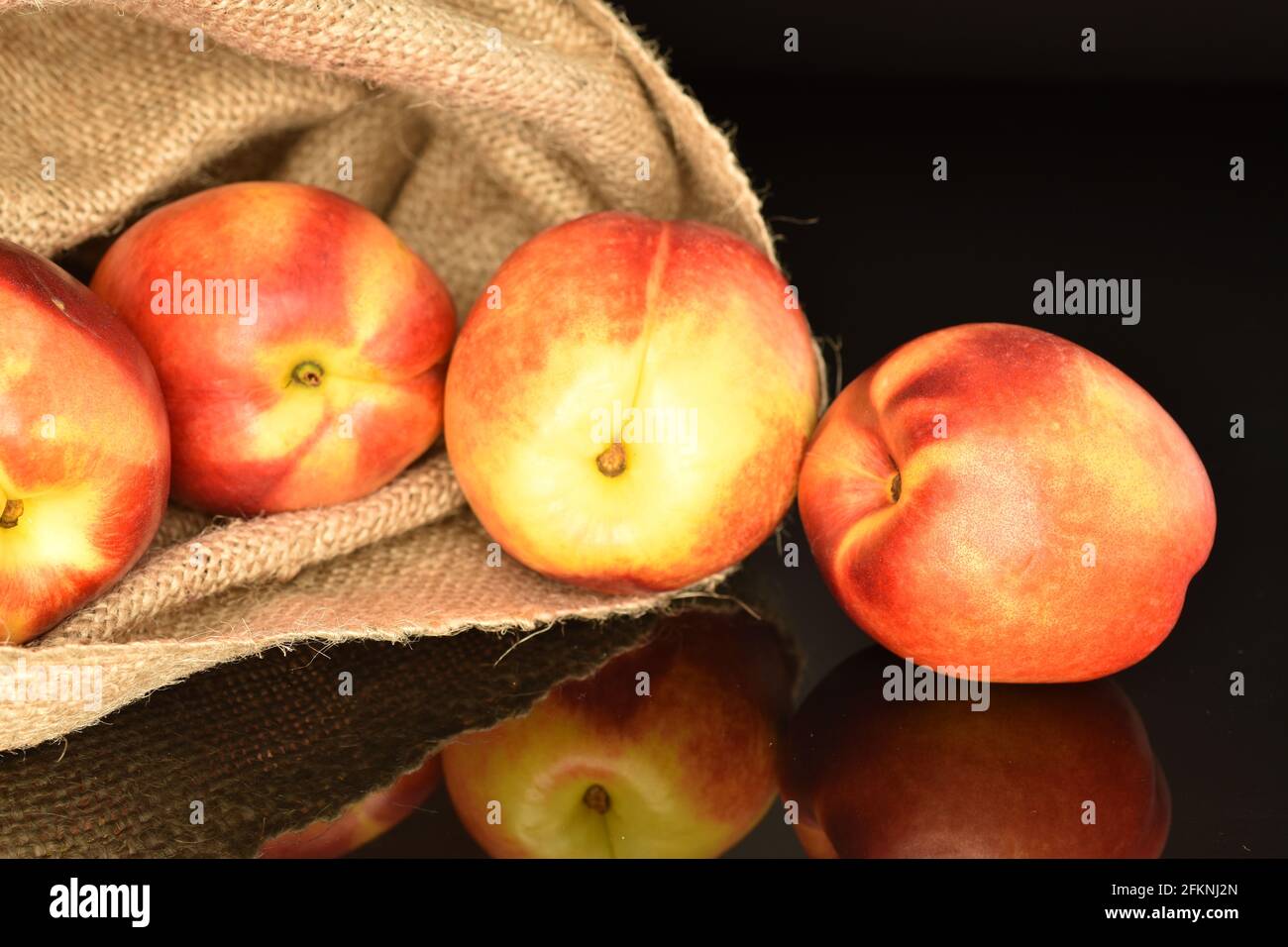 Several fresh nectarines with a jute bag, close-up, on a black background. Stock Photo