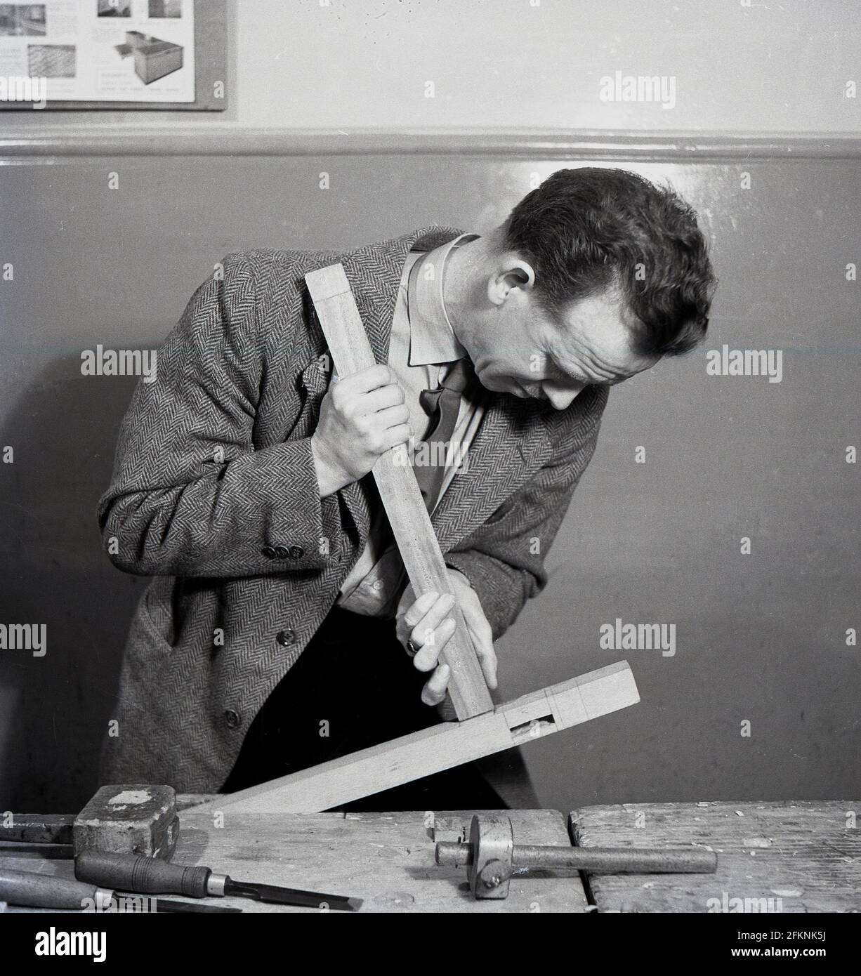 1950s, historical, woodworking, inside a classroom at a bench, a man in a jacket and tie fitting a wooden chair leg to the chair strut  or frame, England, UK. He is attending a an evening woodwork class. Growth and improvement in education became a key political goal in post-war Britain and a large number of adult education colleges were bullt and courses introduced to occupy and retrain ex-servicemen as well as those leaving secondary education. Stock Photo