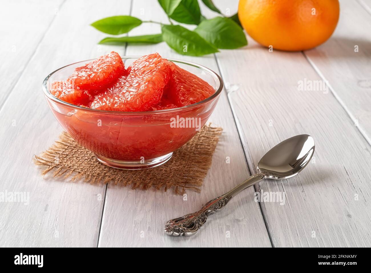 Juicy pulp of ripe pink grapefruit in a glass bowl and spoon on a white wooden table. Tasty vegetarian food, slimming diet and vitamin healthy eating. Stock Photo