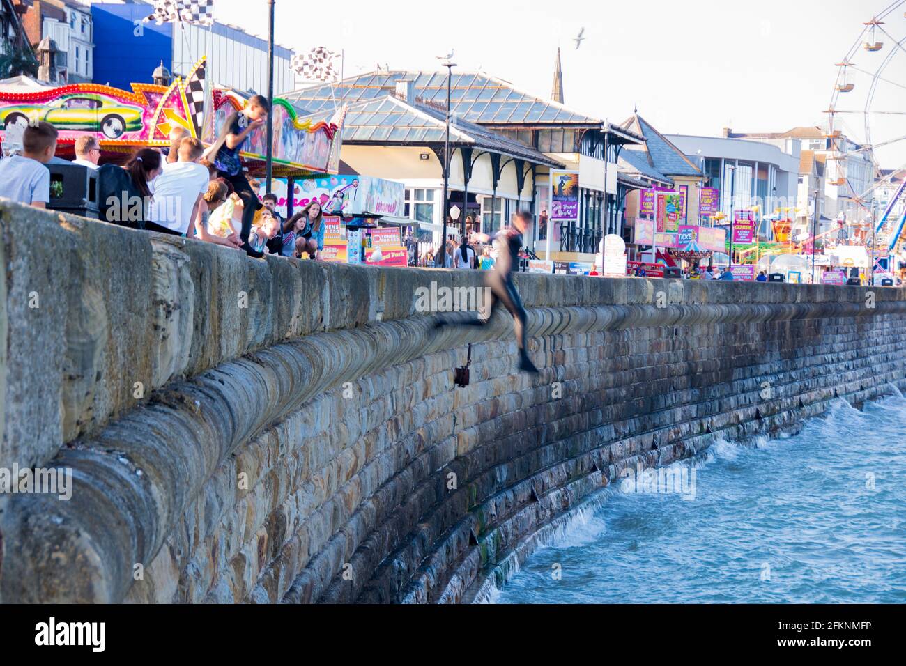 Yorkshire, UK – 10 Aug 2017 : teen boys create dangerous fun jumpng off the sea wall into choppy water at high tide in Bridlington Stock Photo