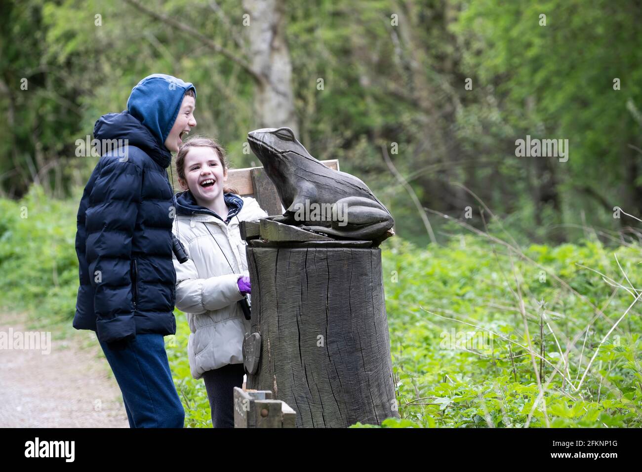 A young boy and girl laughing and enjoying an encounter with a large model of a frog at RSPB Fairburn Ings nature reserve in Yorkshire, U.K. Stock Photo