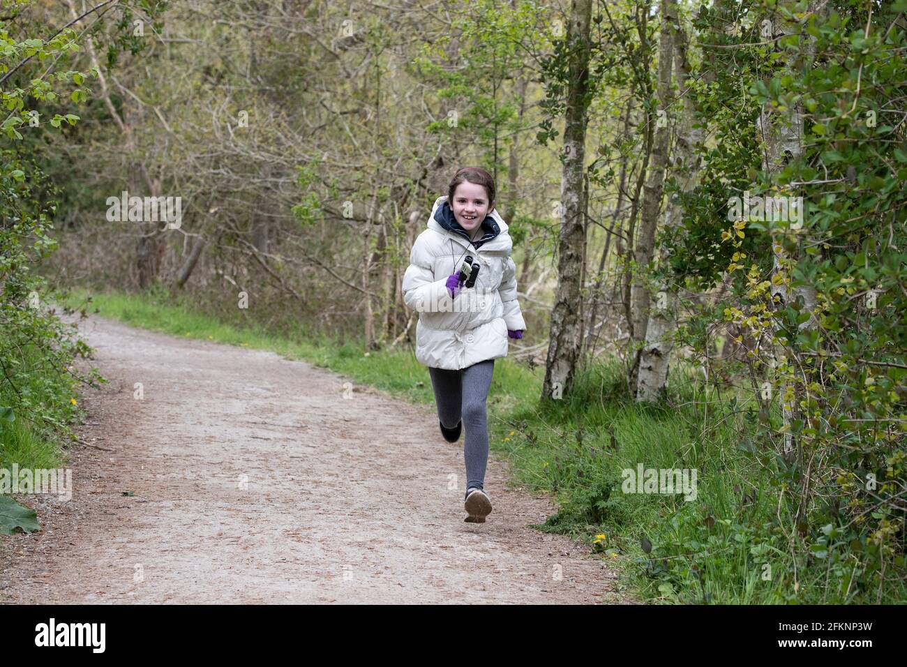 A young girl with binoculars around her neck runs down a tree lined path at RSPB Fairburn Ings, Nature Reserve,Yorkshire U.K. Stock Photo