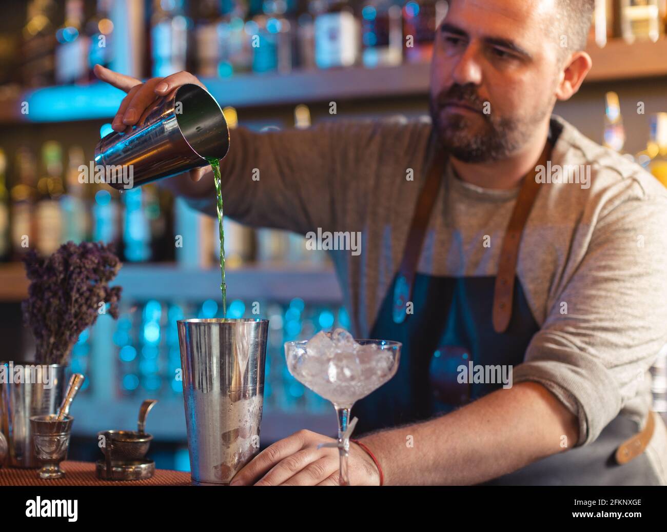 Barman gently pouring beer into shaker on bar counter Stock Photo