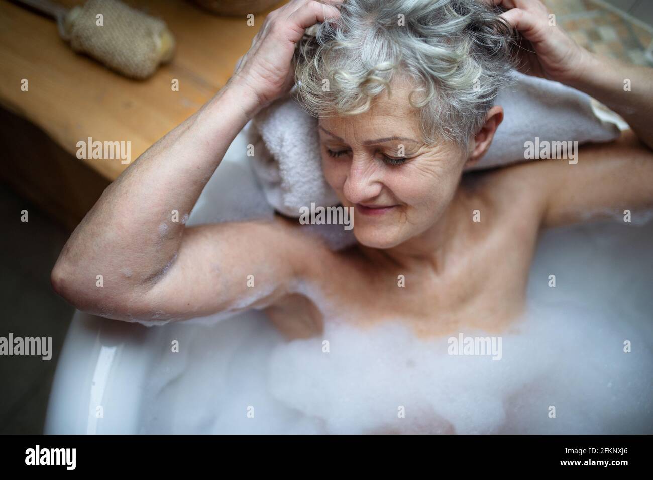Top view of contented senior woman lying in bath tub at home, eyes closed. Stock Photo