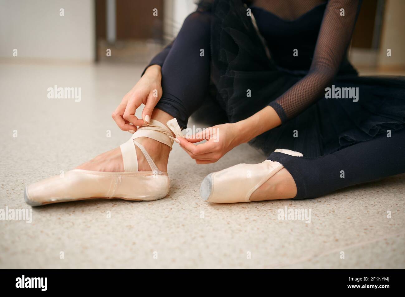 Ballerina sitting on the floor and ties the ribbon Stock Photo