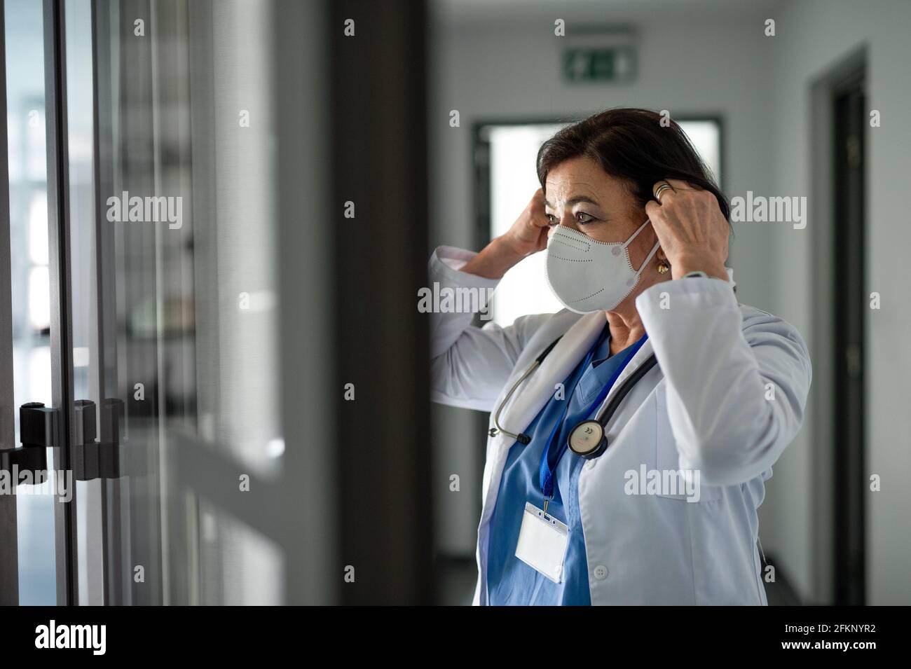 Portrait of senior woman doctor putting on respirator in hospital
