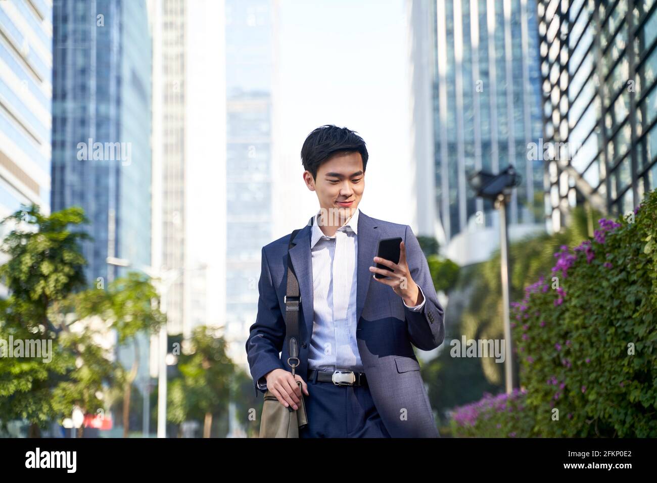 young asian businessman looking at messages on cellphone while walking in the street in downtown of modern city Stock Photo