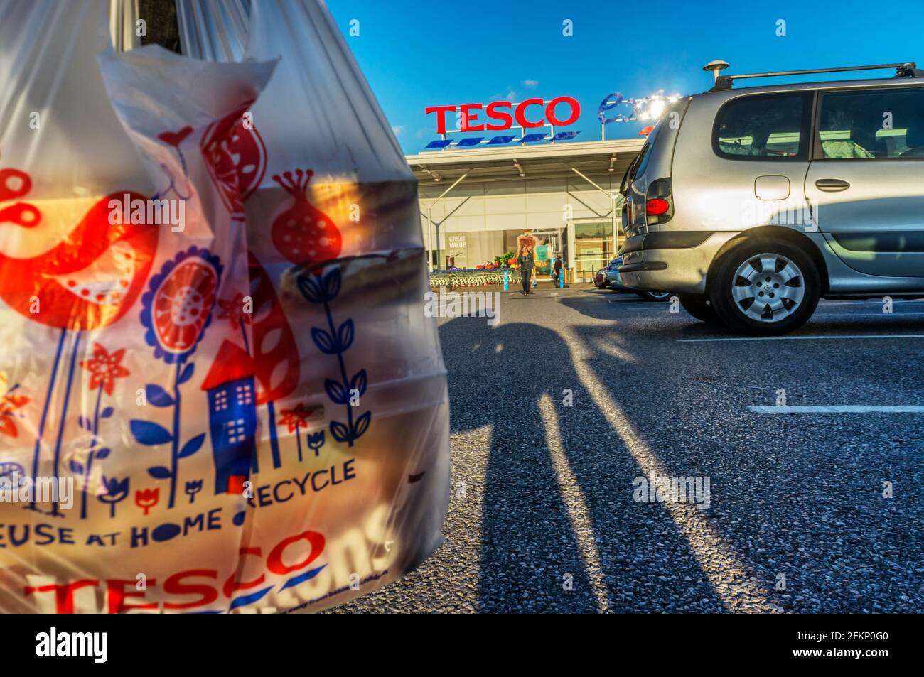 Woman carrying recyclable single use carrier bag with shopping in car park in front of Tesco Extra supermarket. Stock Photo