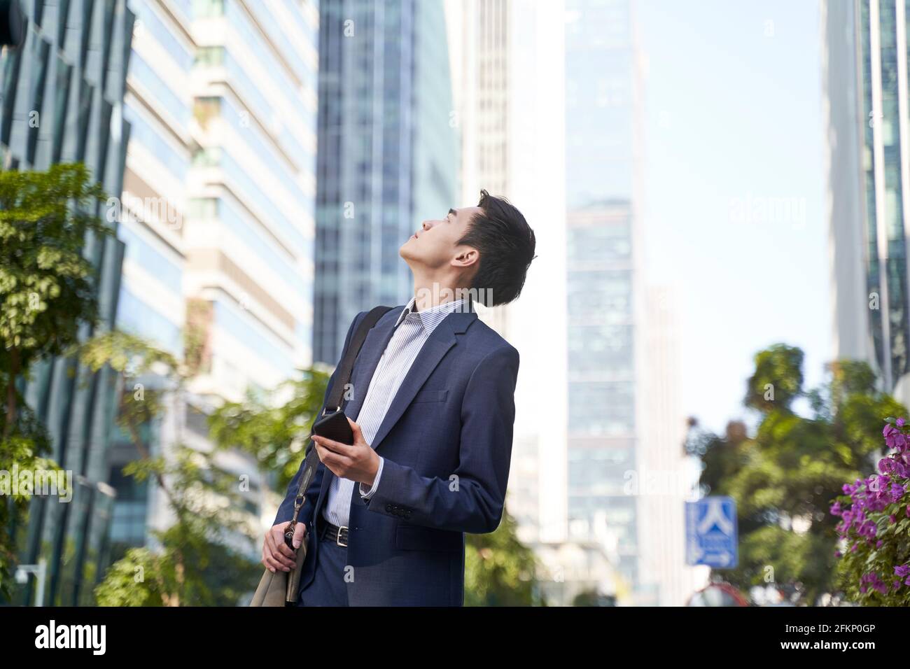 young corporate executive looking up at skyscrapers while walking in street in downtown of modern city Stock Photo