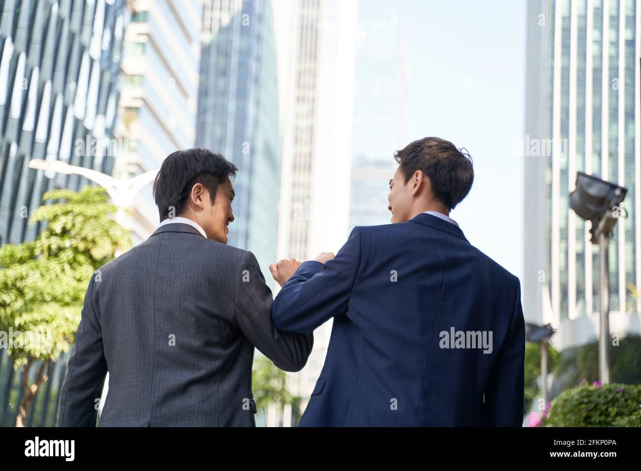 two asian business people bumping elbows celebrating success while walking in street in cbd of modern city Stock Photo