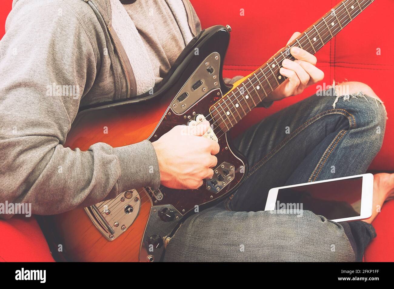 Casual young man in ripped jeans, playing sunburst offset electric guitar.  Young musician taking online musical instrument course lesson on wireless i  Stock Photo - Alamy