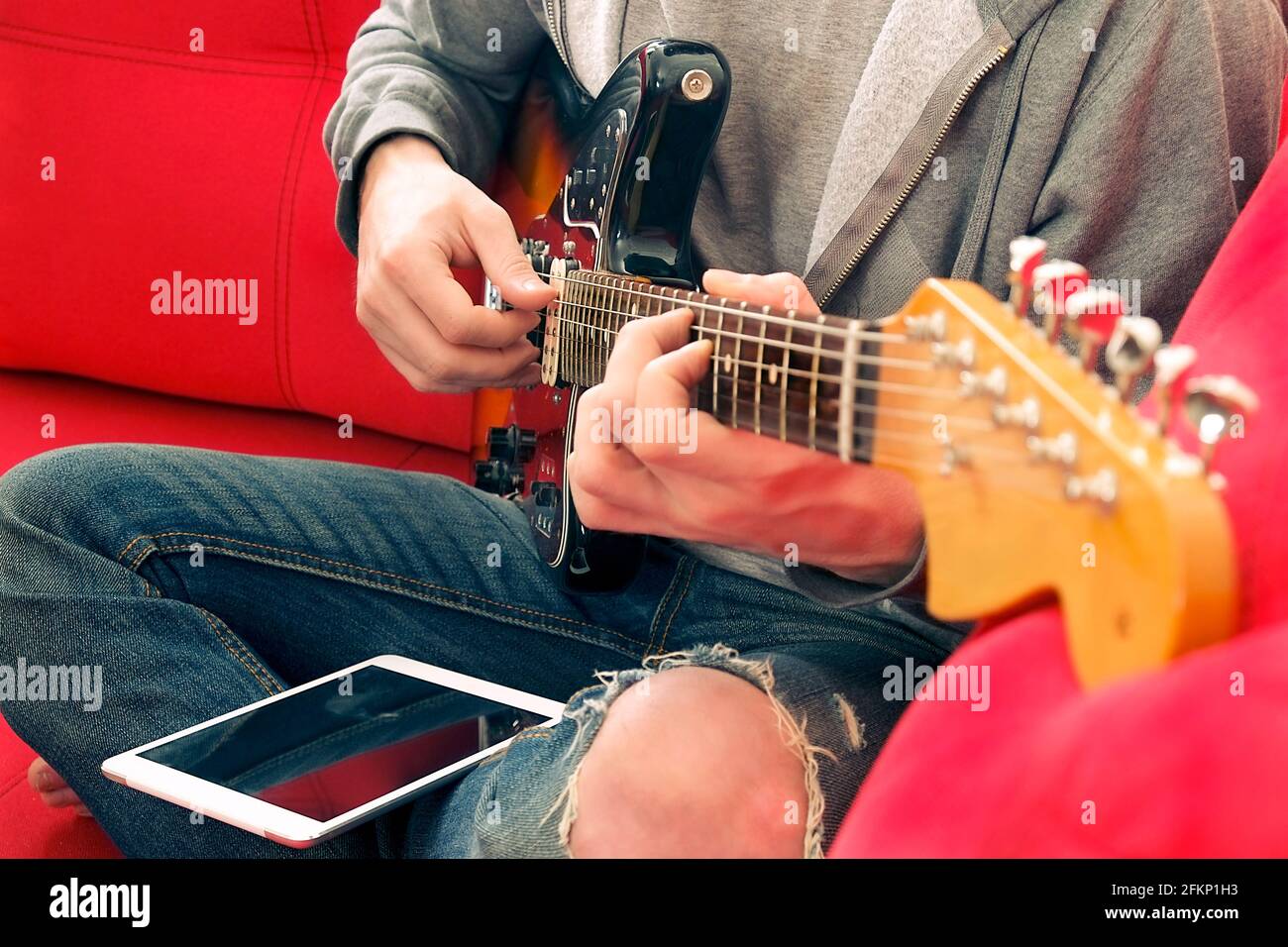 Casual young man in ripped jeans, playing sunburst offset electric